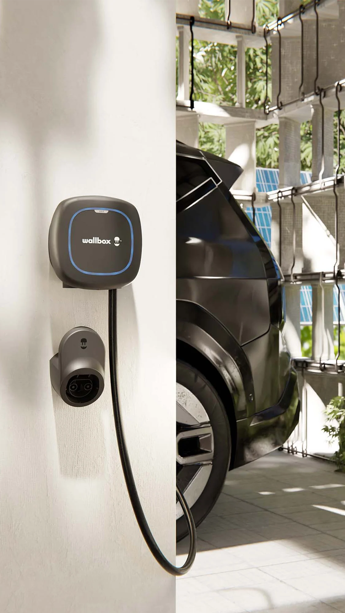 Φορτιστής ηλεκτρικού οχήματος Wallbox Pulsar Max 22kW εγκατεστημένος σε τοίχο γκαράζ, με βάση στήριξης βύσματος και ηλεκτρικό αυτοκίνητο στο φόντο.
